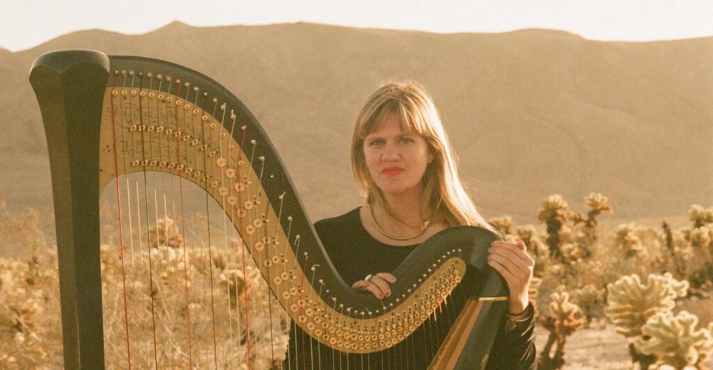 Porträtt Mary Lattimore vid harpa ute i ökenlandskap i USA.