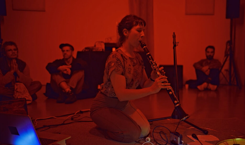 Alexandra Spence playing clarinet sitting on floor in front of electronics during live concert